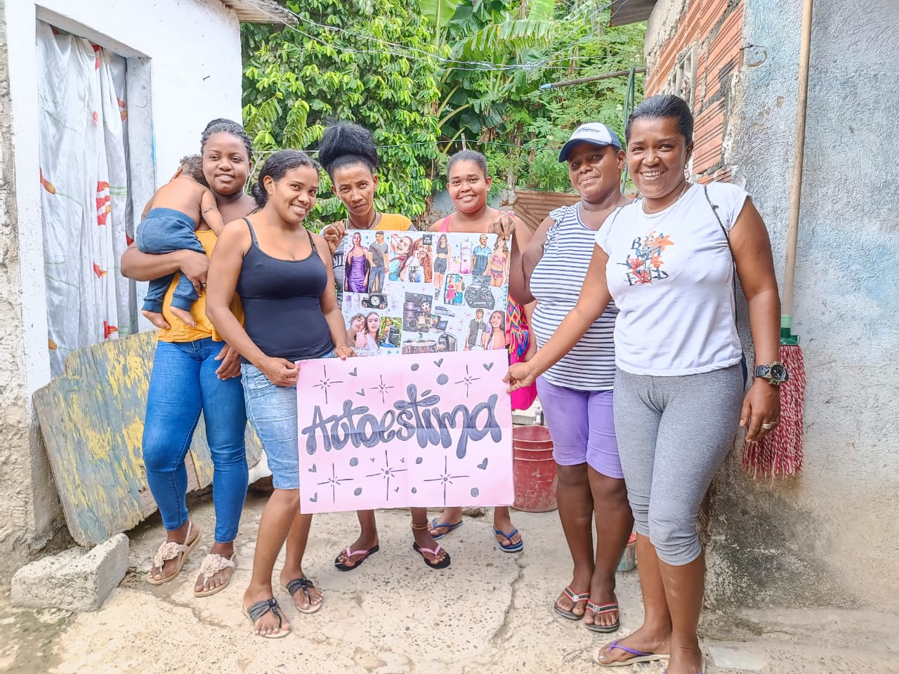 Mujeres participantes del programa Camino de Oportunidades posan con cartel de autoestima durante taller comunitario.