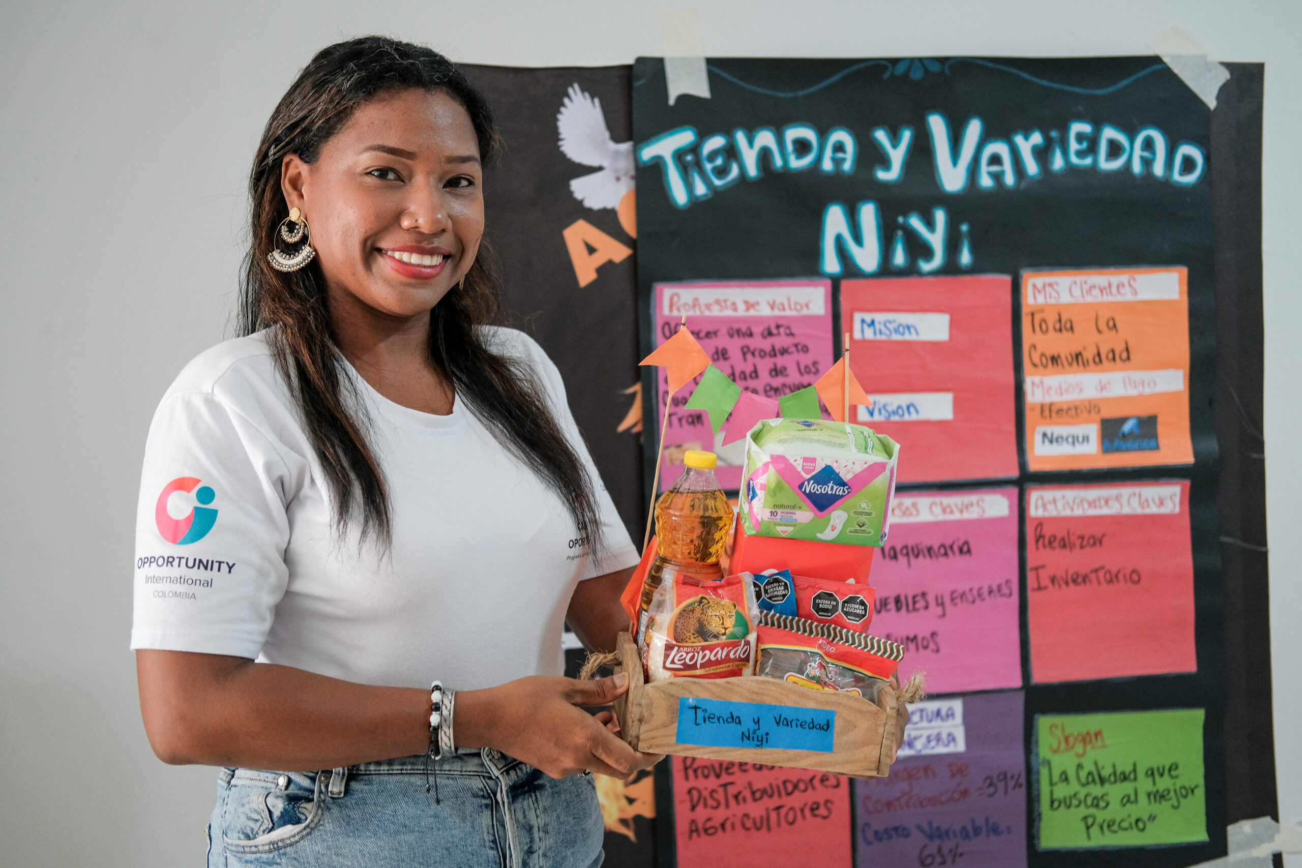 Nillyreth sostiene productos de su negocio comunitario frente a un cartel de emprendimiento.